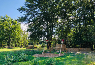 Buitenspeelplaats met houten schommel en strobalen omringd door bomen bij La Ferme de Fontenille.