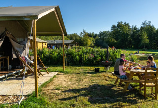 Gezin eet samen buiten aan een tafel naast een tent in Feather Down La Ferme de Fontenille.