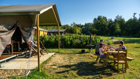 Gezin eet samen buiten aan een tafel naast een tent in Feather Down La Ferme de Fontenille.