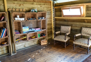 Indvendigt billede af en hyggelig træhytte med bogreoler, to vintage stole og et lille vindue.