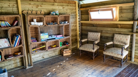 Gezellige houten hut met rieten boekenkasten, twee stoelen met bloemenprint en een klein raam.