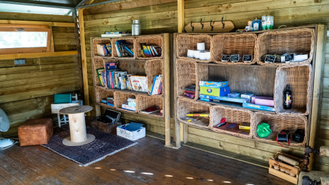 Binnen leeshoek met rieten legplanken gevuld met boeken en spelletjes in Feather Down La Ferme de Fontenille, Canarische Eilanden.