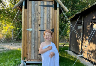 Un bambino sorridente avvolto in un asciugamano bianco davanti a una capanna di legno in un parco vacanze.