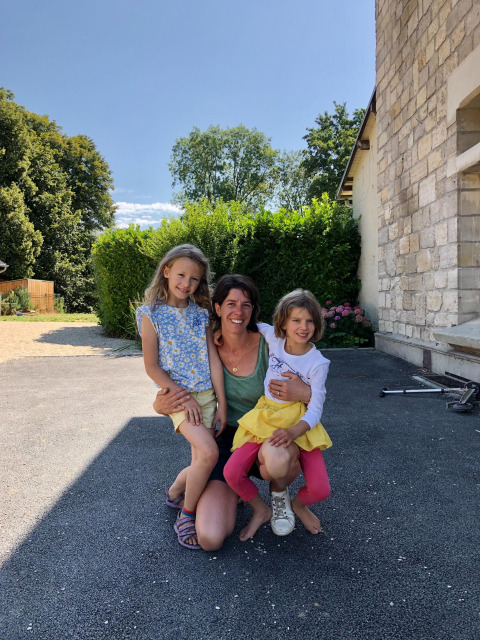 A mother with her two daughters smiling outside in front of a stone house at Feather Down La Ferme de Fontenille, Spain.