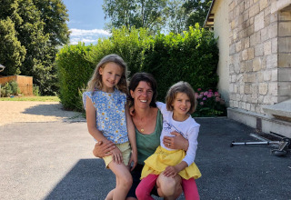 Una madre y sus dos hijas sonríen al aire libre frente a una casa de piedra en Feather Down La Ferme de Fontenille, España.
