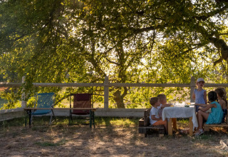 Kinder sitzen an einem Tisch unter einem Baum im Feather Down La Ferme de Fontenille Ferienpark, Spanien.