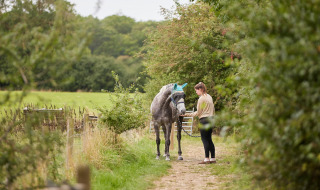 Femme promenant un cheval sur un chemin vert à Feather Down New Barn Farm, parc de vacances en Angleterre.