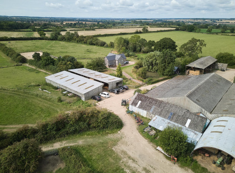 Vista aerea di Feather Down New Barn Farm nell'Est dell'Inghilterra con fienili, campi e alloggi per vacanze.