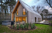 Stijlvolle lodge met jacuzzi, grote ramen en houten gevel in groene, bosrijke omgeving bij schemering.