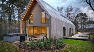 Moderno lodge con jacuzzi, ampie vetrate ed esterno in legno immerso in un paesaggio boschivo al tramonto.