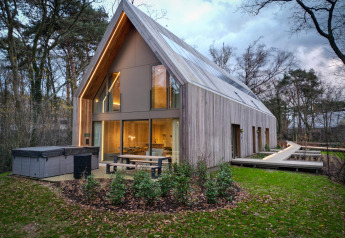 Stijlvolle lodge met jacuzzi, grote ramen en houten gevel in groene, bosrijke omgeving bij schemering.