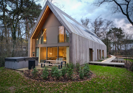 Moderne lodge met jacuzzi, grote ramen en houten gevel, gelegen in een rustige bosrijke omgeving bij schemer.