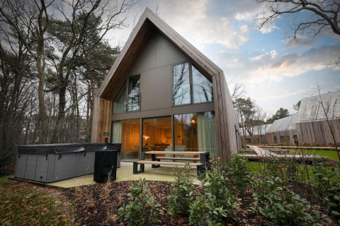 Modern lodge with jacuzzi and large windows at Woodz Lodges in Belgium, surrounded by forest scenery.