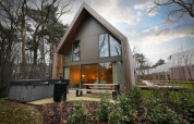 Moderne lodge met jacuzzi en grote ramen bij Woodz Lodges in België, omgeven door bos en groen.