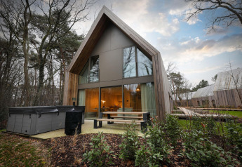 Moderne lodge met jacuzzi en grote ramen bij Woodz Lodges in België, omgeven door bos en groen.