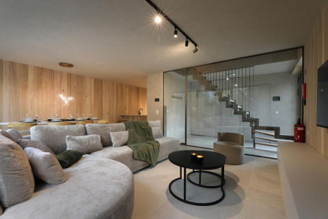 Sala de estar moderna en lodge con paredes de madera clara, gran sofá, comedor y escalera acristalada.