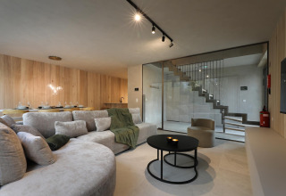 Sala de estar moderna en lodge con paredes de madera clara, gran sofá, comedor y escalera acristalada.