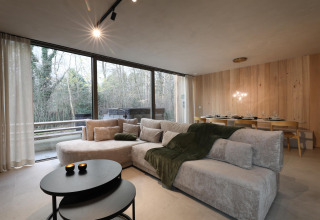 Moderna cabaña con jacuzzi en Woodz Lodges, Bélgica; sala espaciosa, sofá, mesa de comedor y vista al bosque.