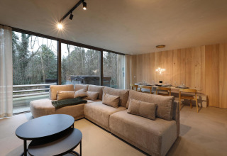 Salón moderno de cabaña con sofá acogedor, mesa de comedor y grandes ventanales en Lodge con Jacuzzi en Woodz Lodges, Bélgica.