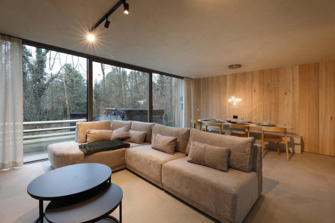 Salón moderno de cabaña con sofá acogedor, mesa de comedor y grandes ventanales en Lodge con Jacuzzi en Woodz Lodges, Bélgica.