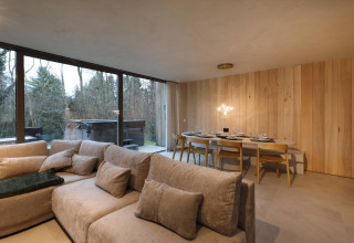Sala de estar y comedor en Lodge con Jacuzzi en Woodz Lodges, Bélgica, con vistas al bosque a través de grandes ventanales.