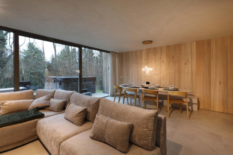 Wohn- und Essbereich der Lodge mit Jacuzzi bei Woodz Lodges in Belgien mit Blick auf den Wald durch Panoramafenster.