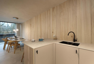 Modern lodge kitchen with light wood paneling, black faucet, dining area and large window to nature.