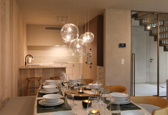 Moderne Esszimmer in einer Lodge mit gedecktem Tisch, Glaslampen, Küche und Treppe im Hintergrund.