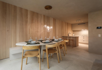 Moderne lodge-eetkamer met houten stoelen, glazen hanglampen en open keuken met lichte wandpanelen.