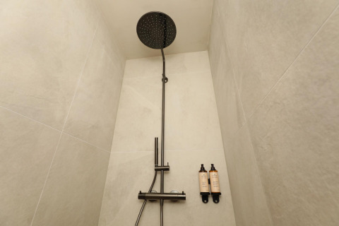 Modern shower at a lodge, featuring a large black rainfall showerhead and two mounted soap bottles.