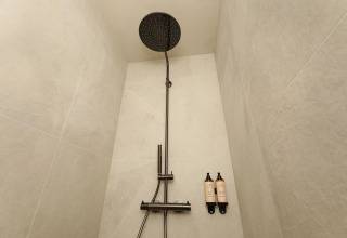 Ducha moderna en un lodge, con cabezal de lluvia negro grande y dos botellas de jabón montadas en la pared.