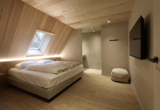 Habitación de lodge moderna con cama doble, techo inclinado de madera, ventana grande y televisor mural.