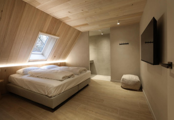 Moderne lodgekamer met tweepersoonsbed, schuine houten wand, dakraam, poef en grote muur-tv.