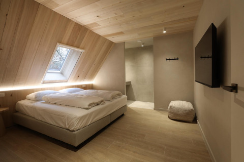 Modern lodge bedroom with a double bed, slanted wood ceiling, skylight window, pouf, and a wall-mounted TV.