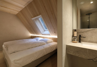 Foto de un dormitorio moderno en una cabaña con techo inclinado, ventana tragaluz y baño contiguo.
