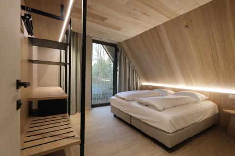 Habitación moderna de lodge con paneles de madera, cama doble, ventana grande e interior minimalista.