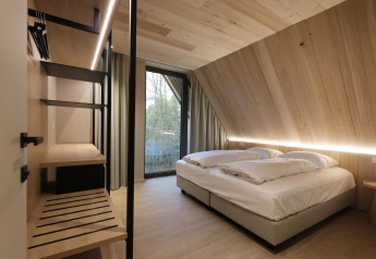 Modern lodge room with wood paneling, a double bed, large window and minimalist stylish interior decor.