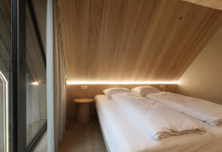 Dormitorio acogedor en una cabaña con techo inclinado de madera, dos camas individuales y luz LED suave.
