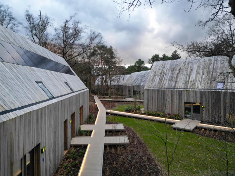Billede af moderne lodgebygninger med træfacader og gangbroer, omgivet af skov og grønne områder.