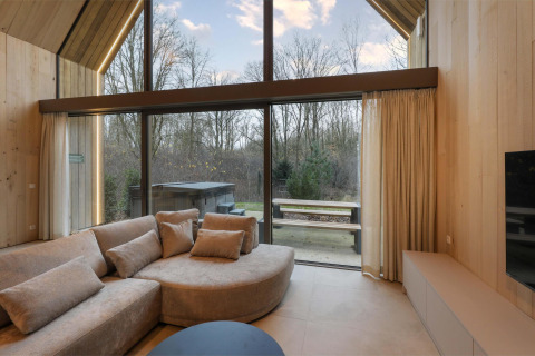 Cozy lodge living room with large windows, sofa, and view of outdoor jacuzzi and forest scenery.