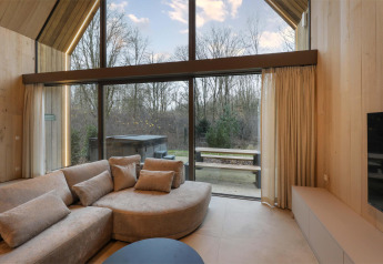 Gezellige lodge woonkamer met grote ramen, comfortabele zetel en zicht op jacuzzi en natuur.