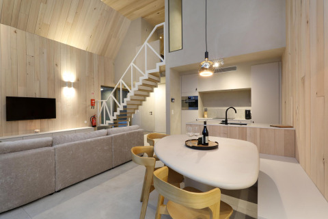 Interior de lodge moderno con cocina abierta, comedor, escalera, sofá cómodo y televisor en la pared.