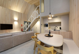 Interior de lodge moderno con cocina abierta, comedor, escalera, sofá cómodo y televisor en la pared.