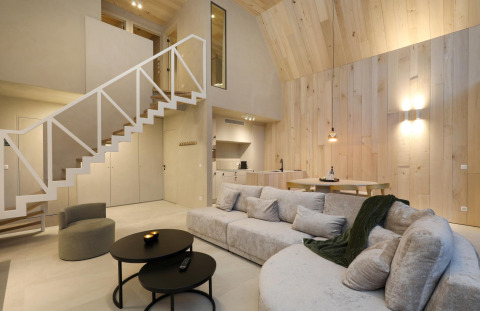 Modern lodge interior with bright wood walls, cozy sectional sofa, open kitchen area, and loft stairs.