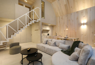 Modern lodge interior with bright wood walls, cozy sectional sofa, open kitchen area, and loft stairs.
