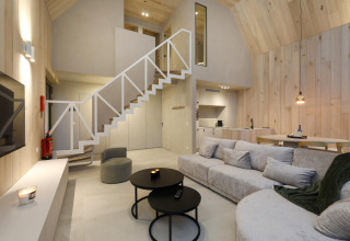 Acogedora cabaña moderna con paneles de madera clara, sofá grande, escalera abierta y cocina integrada.