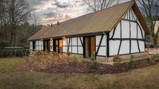 Villa Lodge met jacuzzi in traditionele vakwerkstijl, omgeven door tuin en natuur bij avondlicht.