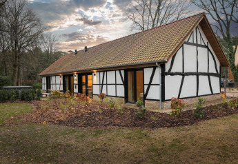 Charmerende Villa Lodge med traditionel arkitektur og jacuzzi, omringet af træer og have ved solnedgang.