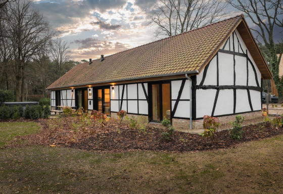 Villa Lodge met jacuzzi in traditionele vakwerkstijl, omgeven door tuin en natuur bij avondlicht.