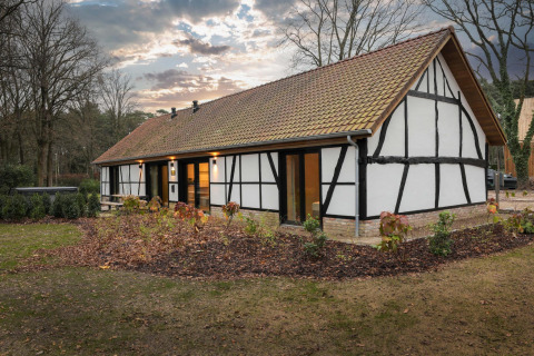 Villa Lodge with Jacuzzi, featuring traditional timber framing, surrounded by gardens and nature at dusk.